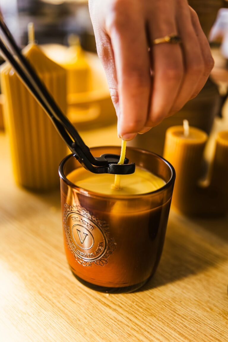 Mano recortando la mecha de una vela de cera de abeja en vaso &aacute;mbar con un cortamechas