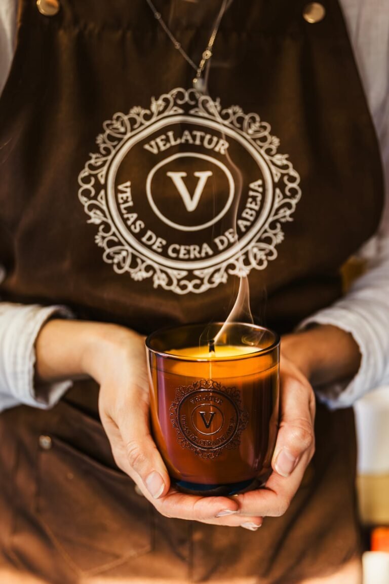 Manos sosteniendo una vela de cera de abeja encendida en vaso de cristal &aacute;mbar
