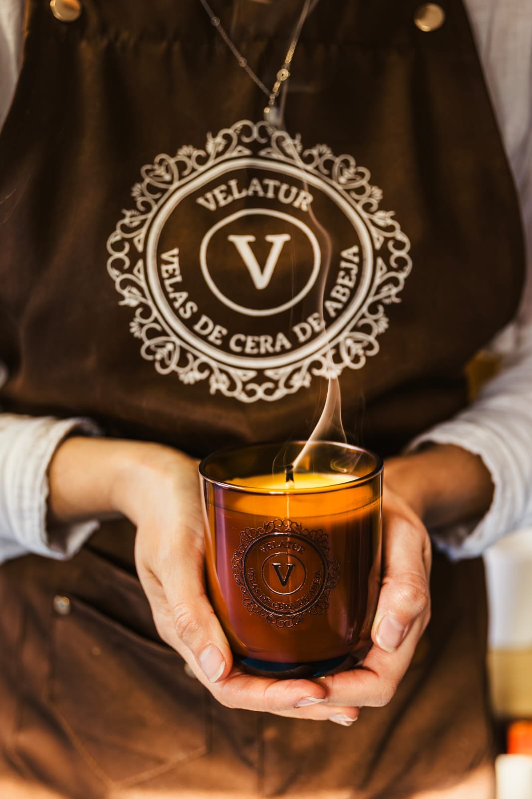 Vela de cera de abeja en vaso de cristal &aacute;mbar sostenida a mano