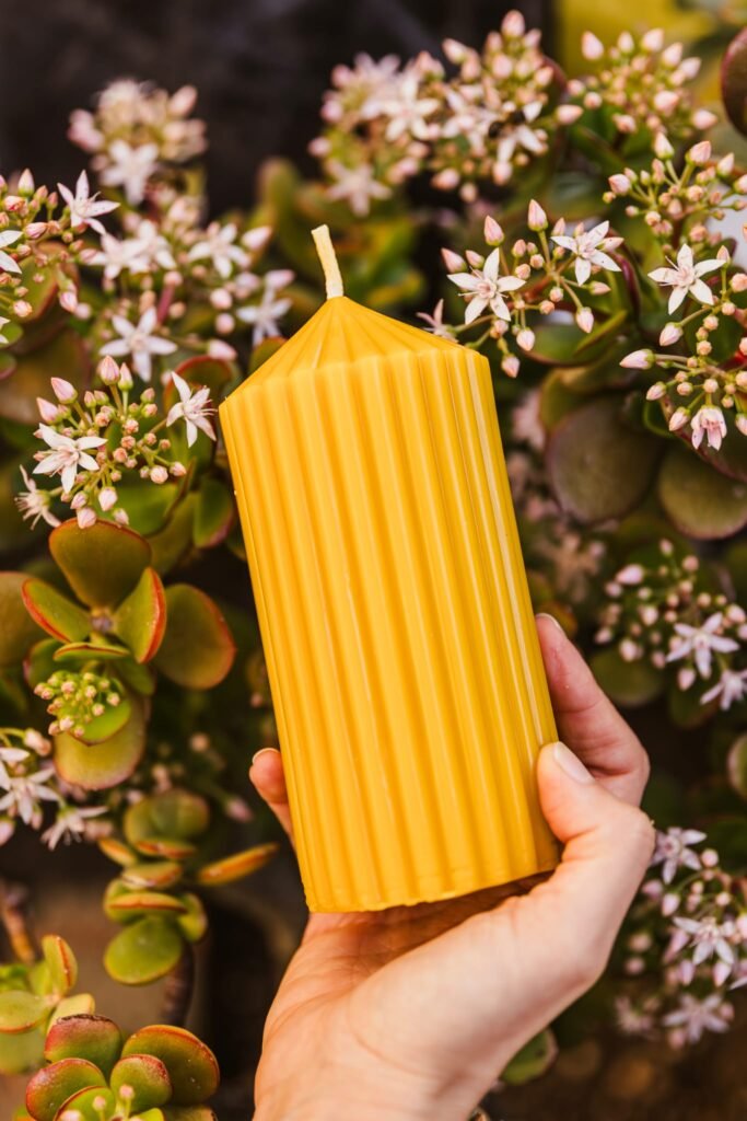 Vela decorativa acanalada de cera de abeja amarilla sostenida entre flores