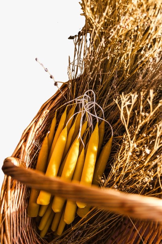 Cesta de mimbre con velas finas de cera de abeja atadas, entre espigas secas