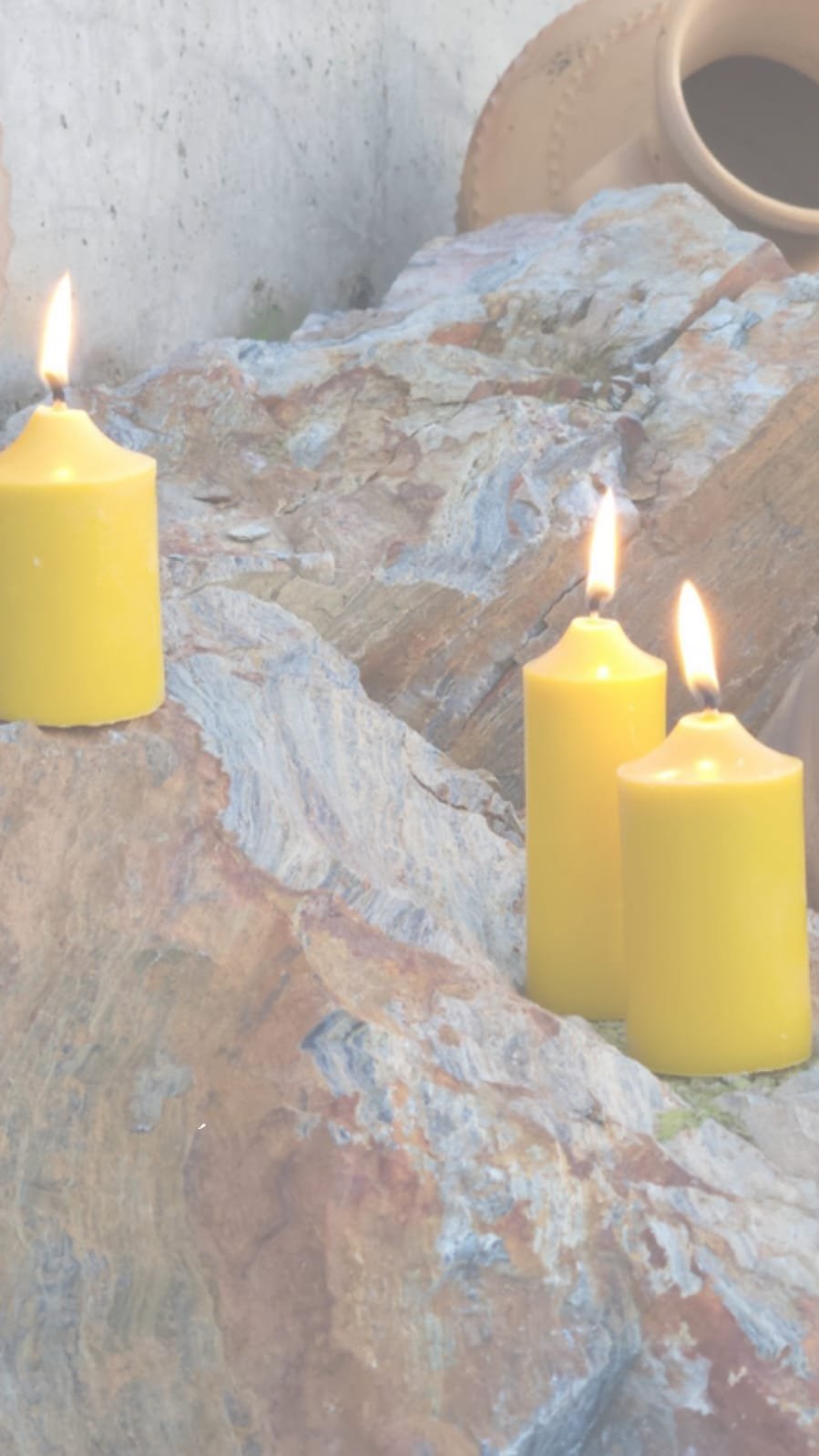 Tres velas de cera de abeja encendidas sobre una roca, junto a una vasija de barro