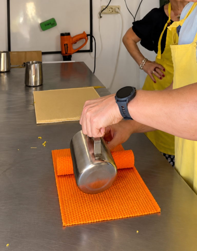 Enrollando una l&aacute;mina de cera de abeja naranja para hacer una vela de panal en el taller